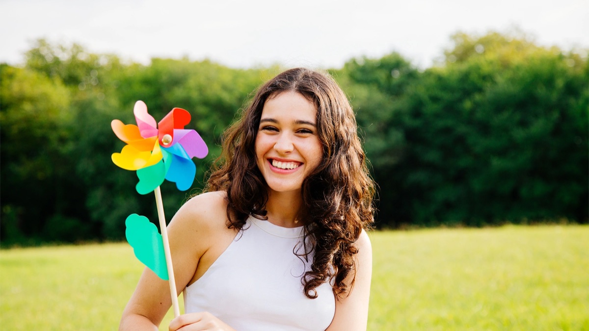 A smiling young woman holding a pinwheel in a park