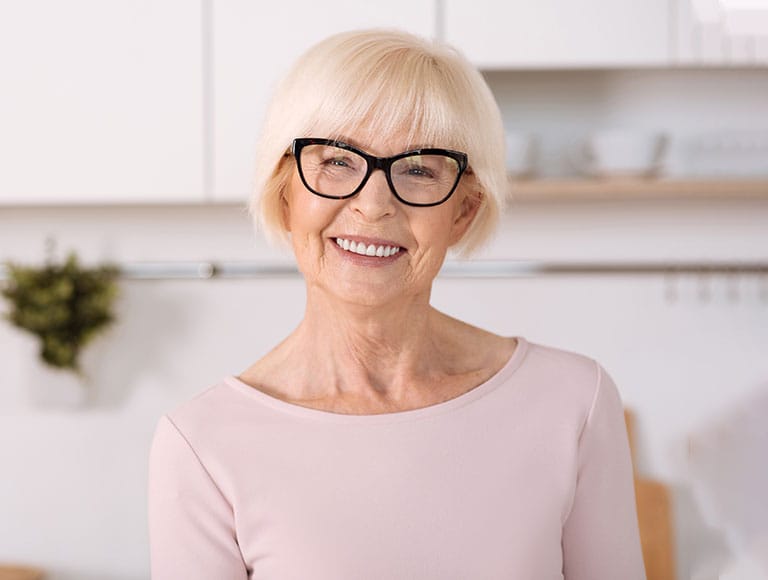 A smiling older woman with glasses in a bright kitchen