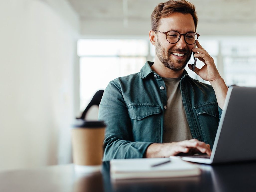 A man smiling as he talks on the phone at his desk