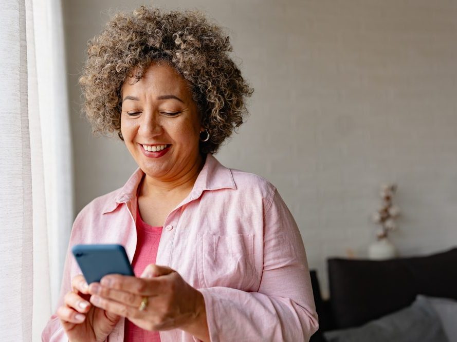 A woman smiling as she looks at her phone at home