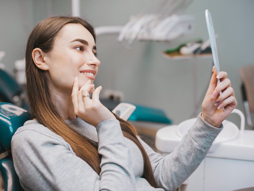 A patient admiring her smile in a hand mirror in the dental chair
