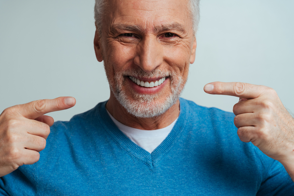 A happy older man pointing at his healthy teeth, representing renewed confidence with dental implants - Dental Implants Rancho Bernardo