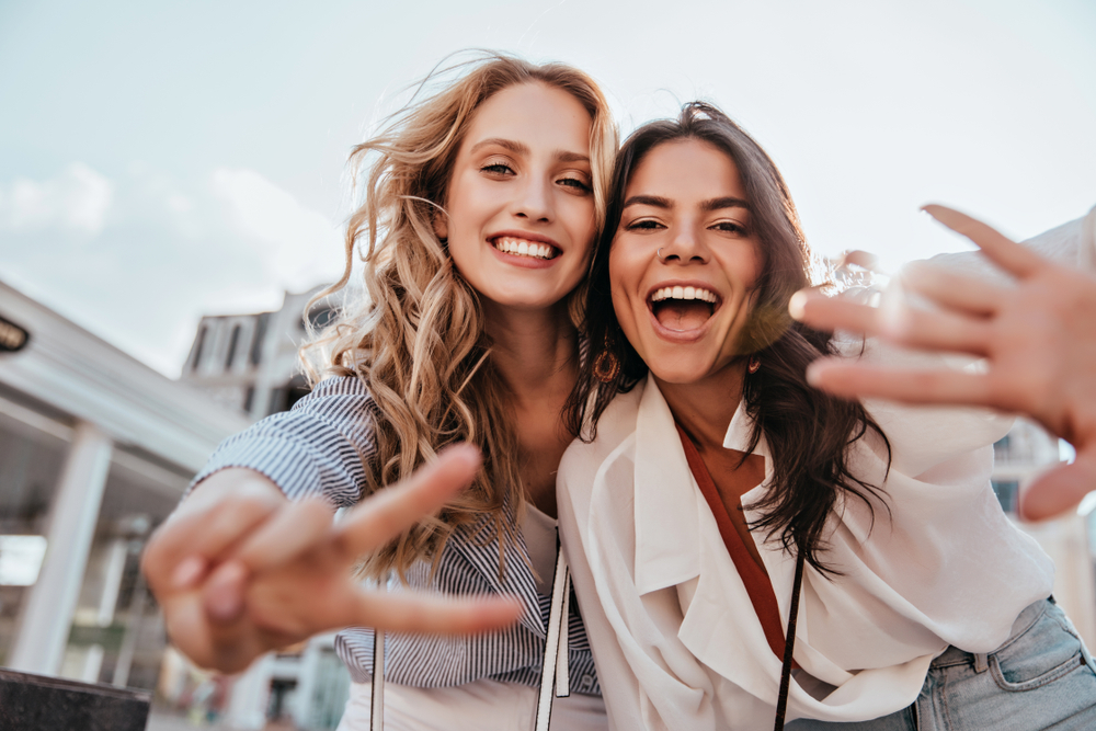 Two cheerful young women enjoying time together outdoors, showing off radiant smiles after professional teeth whitening - Teeth Whitening Rancho Bernardo