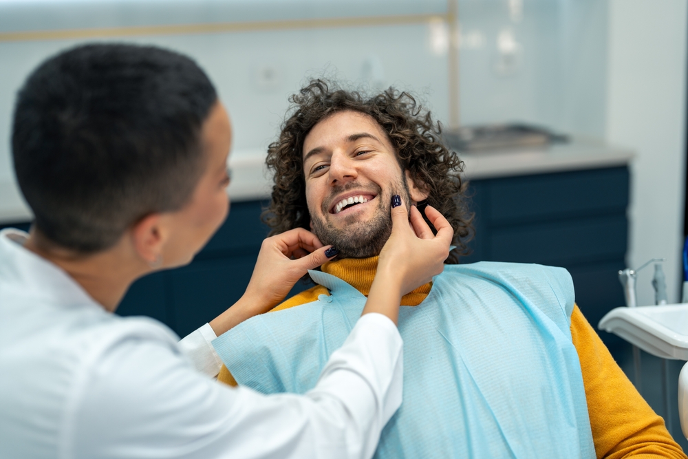 Dentist examining smiling patient - Tooth Extraction Rancho Bernardo A man sitting in the dental chair smiling as the dentist checks his teeth, showing comfort and trust before treatment - Tooth Extraction Rancho Bernardo