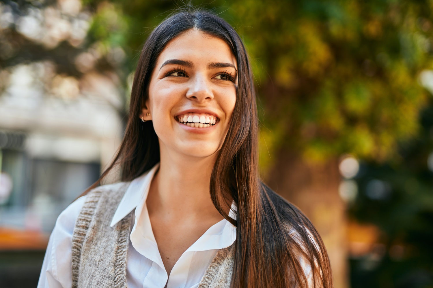 Confident woman smiling outdoors after dental implants - Anchor Dental & Implant Center Young woman with bright smile standing outside, representing successful dental implants - Anchor Dental & Implant Center