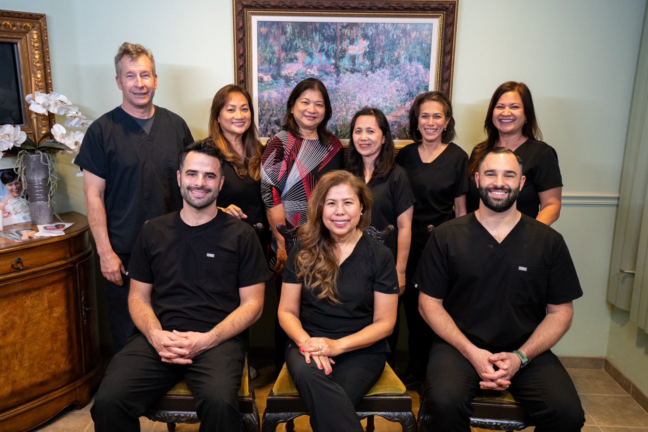 Friendly dental team group photo in office – Anchor Dental & Implant Center Smiling team of dental professionals in black uniforms posing together inside the office, showcasing a welcoming staff – Anchor Dental & Implant Center