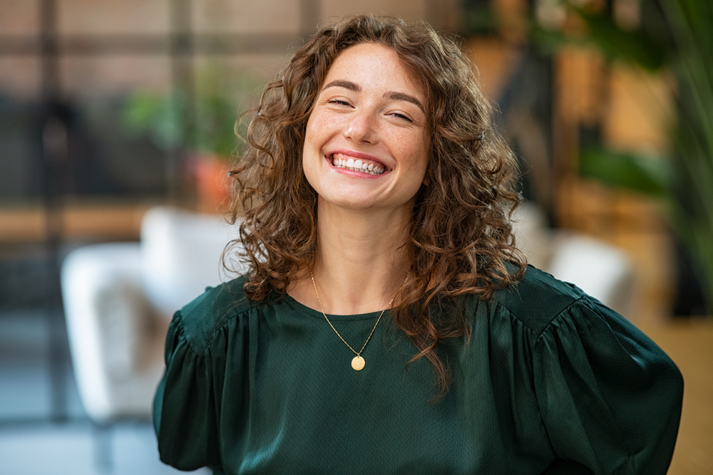 Smiling woman with healthy teeth indoors - Rancho Bernardo Dentist Young woman with curly hair smiling brightly, showing confidence after dental care - Rancho Bernardo Dentist