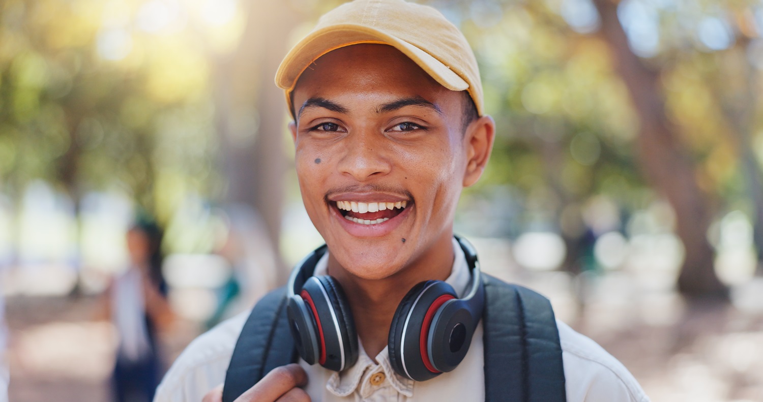 Young man smiling confidently after teeth whitening - Anchor Dental & Implant Center Happy young man outdoors with headphones, showing bright white smile after teeth whitening - Anchor Dental & Implant Center