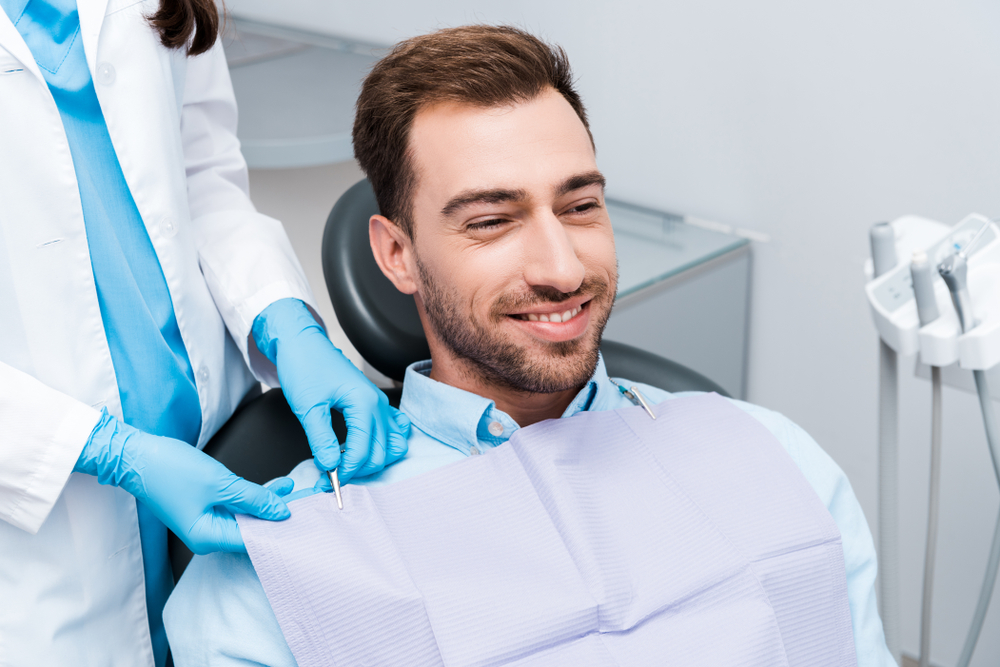Patient preparing for dental treatment - Tooth Extraction Rancho Bernardo A male patient sitting in a dental chair with a bib on, ready for his dental procedure - Tooth Extraction Rancho Bernardo