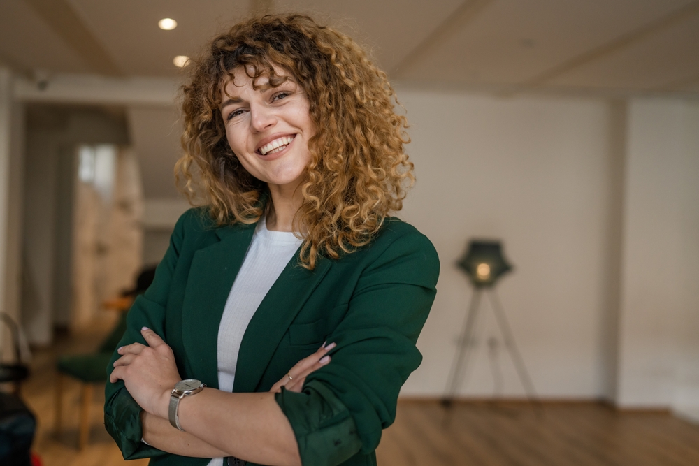 Confident woman smiling after veneers treatment - Rancho Bernardo Dentist Young woman with curly hair smiling indoors, showing perfect teeth from veneers - Rancho Bernardo Dentist