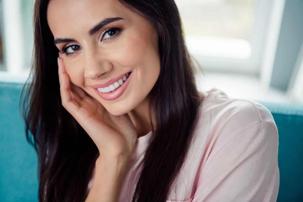 A young woman resting her hand on her cheek, confidently showing her bright, white smile after whitening treatment - Teeth Whitening Rancho Bernardo