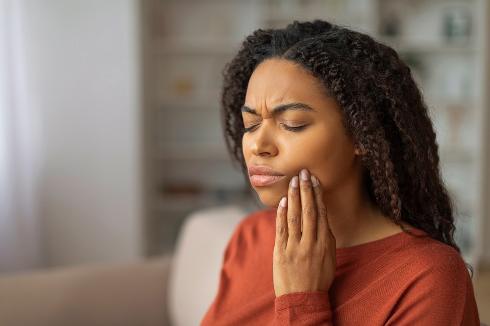 Woman holding cheek in pain showing dental emergency - Anchor Dental & Implant Center Young woman experiencing severe tooth pain at home, representing dental emergencies - Anchor Dental & Implant Center